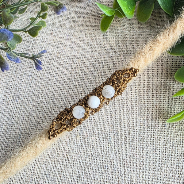 Handgefertigte Dreadröhre aus goldfarbenem Polyestergarn mit Metallicfaden in einem hellen Dread getragen. Drei eingefasste Mondstein-Perlen werden von kleinen antikbronzefarbenen Glasperlen ergänzt und verleihen der filigranen Occhi-Handarbeit einen natürlichen, warmen Look.