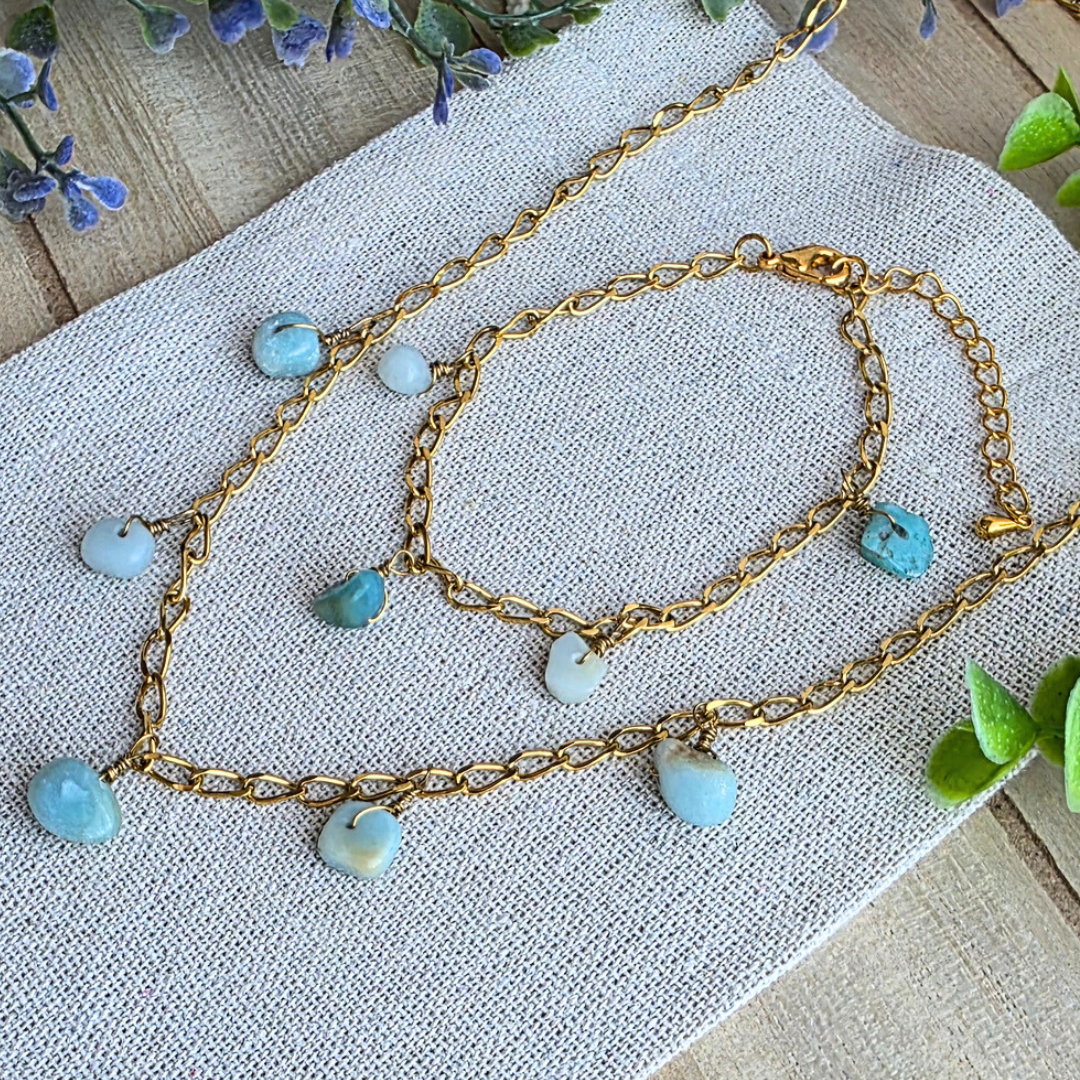 Das komplette MaMari Art Schmuckset aus 24K echtgold-vergoldetem Edelstahl: Halskette und Armband mit passenden Amazonit-Edelsteinen, dekorativ auf Leinen arrangiert.