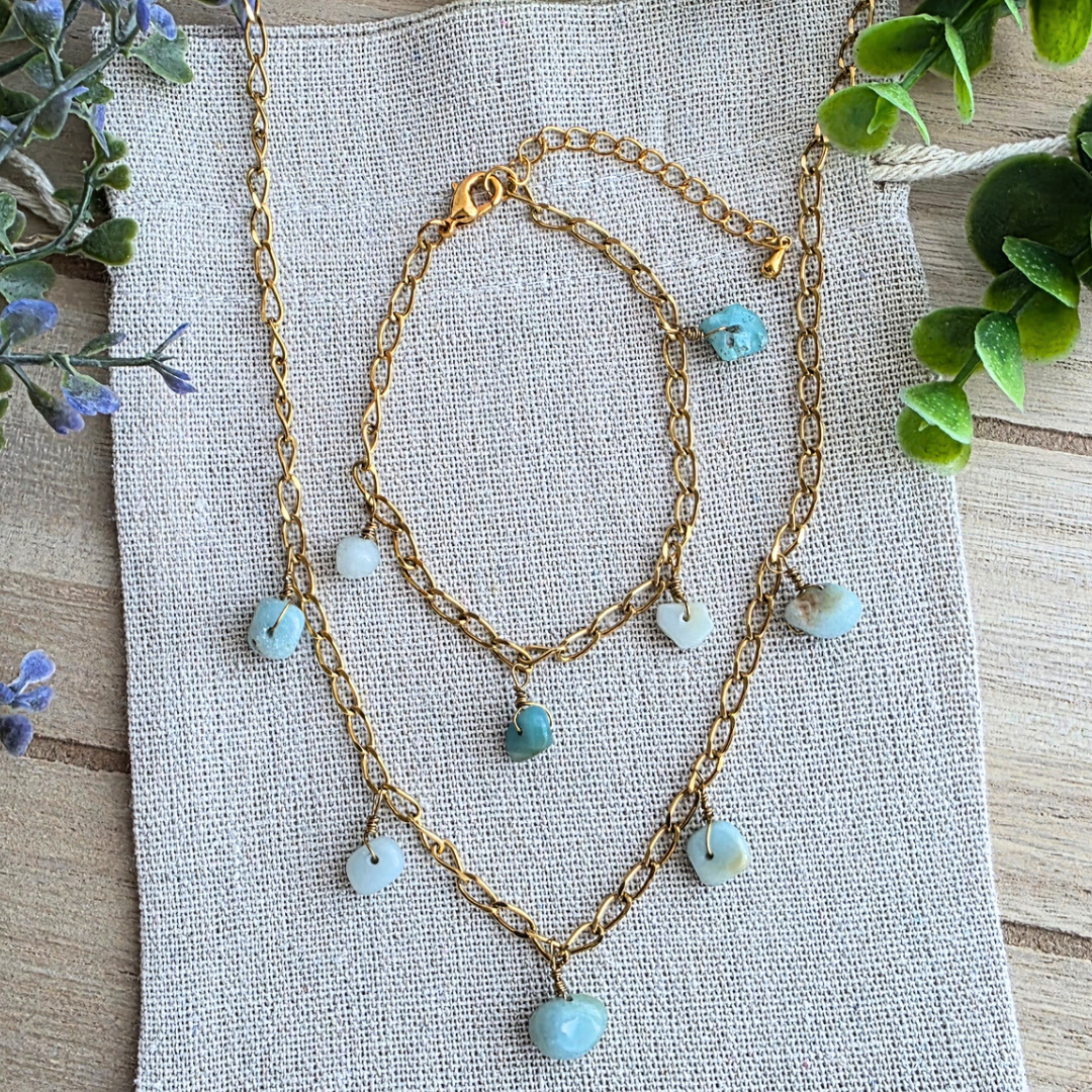Ein handgefertigtes Boho-Schmuckset aus Halskette und Armband mit natürlichen Amazonit-Nuggets in Gold-Edelstahl-Fassung auf hellem Stoffhintergrund.