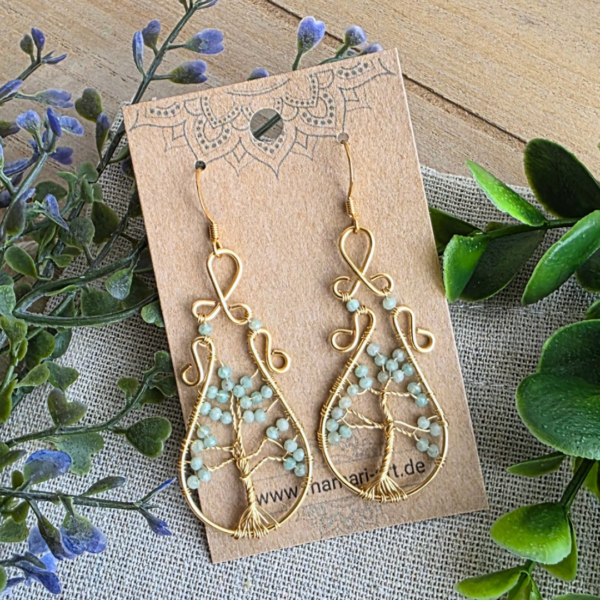 Ein Paar Ohrringe Lebensbaum Amazonit Gold präsentiert auf einem MaMari Art Schmuckkärtchen vor Eukalyptus; zeigt das filigrane Design mit 24k vergoldeten Ohrhaken.