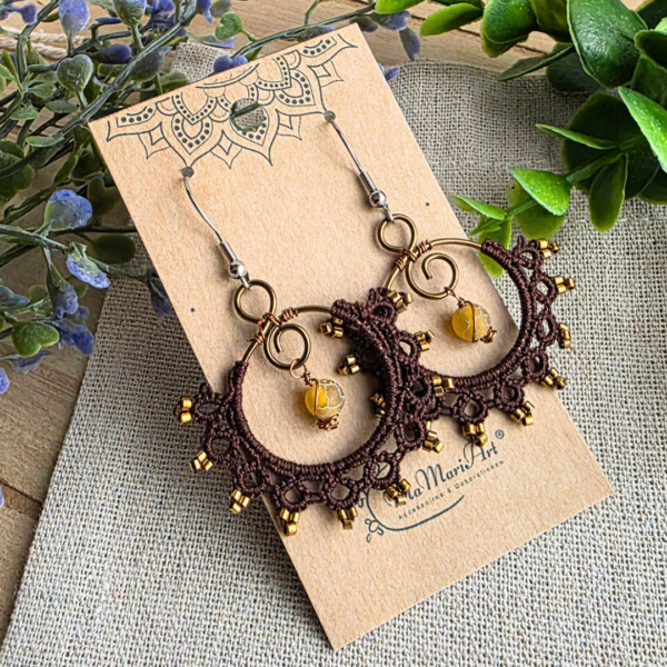 Ein Paar MokkaSun Ohrringe präsentiert auf einem MaMari Art Schmuckkärtchen; zeigt die dunkelbraunen Ornament-Ohrringe mit gelben Edelsteinen vor dekorativem Eukalyptus.