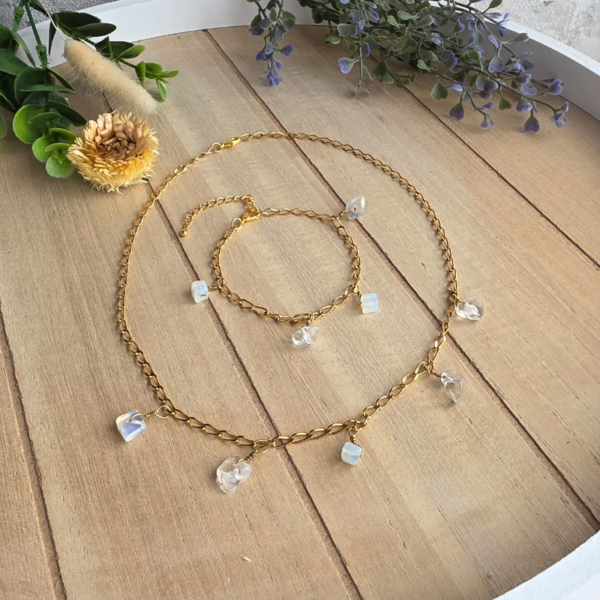 Schmuckset aus goldener Edelstahlkette und Armband mit schimmernden Opalit-Edelsteinen auf hellem Holzgrund.
