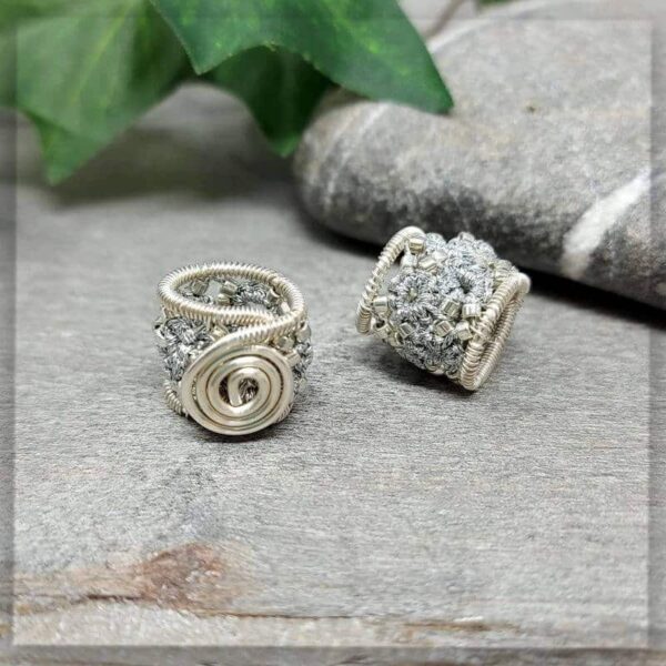 2 Dreadperlen in silber metallic Garn geknotet und mit silbernen Glasperlen verziert, stabilisiert mit silbernem Draht der zu einer Spirale geformt ist