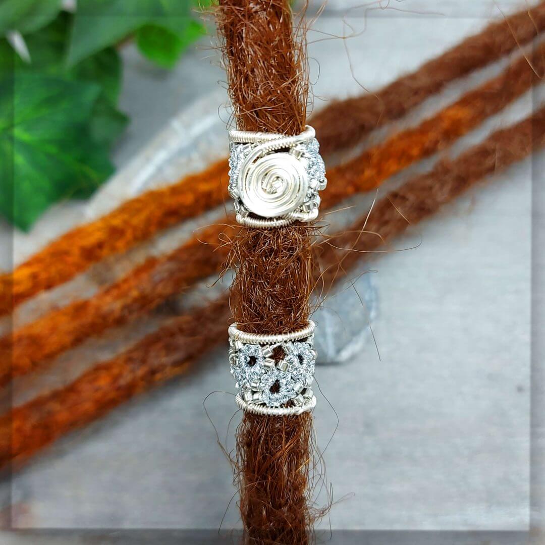 2 Dreadperlen in silber metallic Garn geknotet und mit silbernen Glasperlen verziert, stabilisiert mit silbernem Draht der zu einer Spirale geformt ist