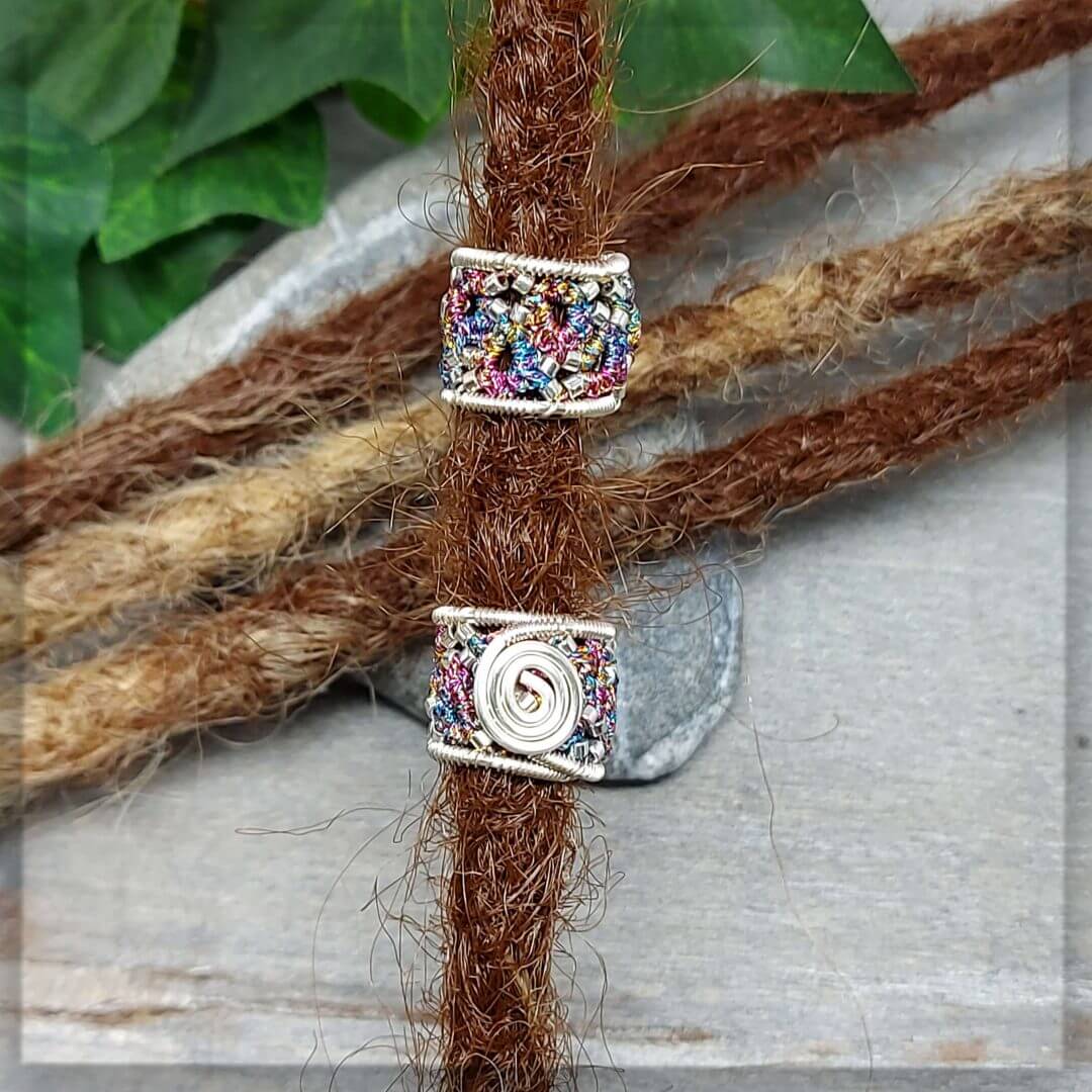 2 Dreadperlen geknotet aus bunten Metallicgarn und silbernen Glasperlen verziert, mit versilbertem Draht stabiliert und vorne zu einer Spirale geformt