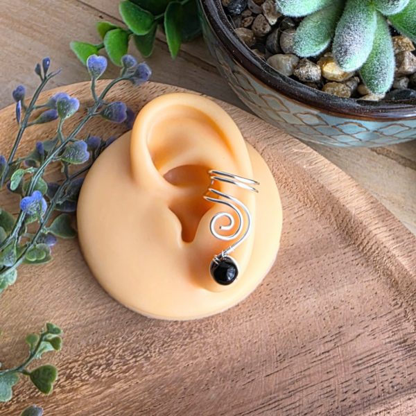 Ear Cuff Vortex in Silber mit schwarzem Onyx an einem Ohrmodell getragen, Ansicht der geschwungenen Drahtform.