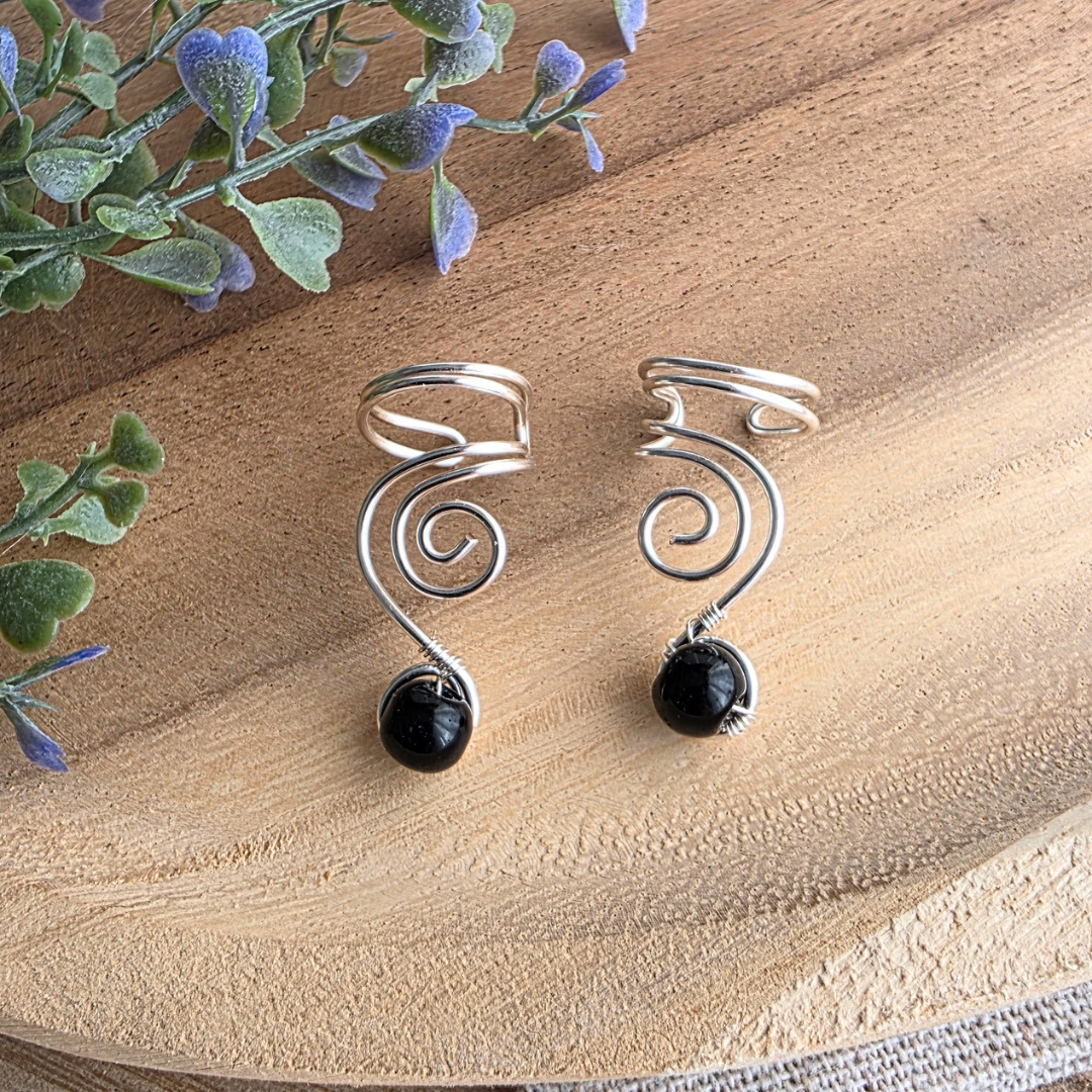 Detailansicht von zwei handgefertigten Ear Cuffs Vortex aus silberfarbenem Draht mit schwarzen Onyxperlen.