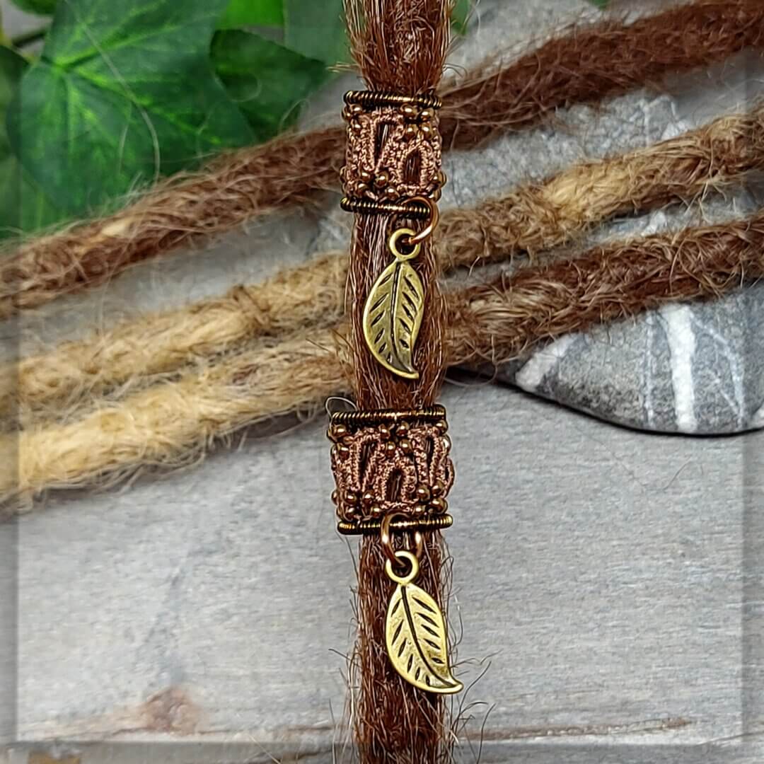 Dreadperlen aus dunkelbraunem Garn geknotet mit antikbronze Draht geformt und mit antikbronze Glasperlen sowie einem Anhänger als Blatt verziert