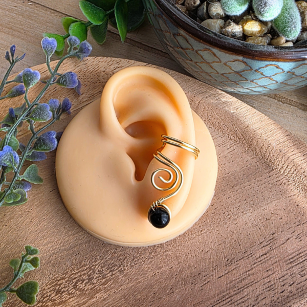 Trageansicht des goldfarbenen Ear Cuffs Vortex mit Spirale und schwarzer Onyxperle an einem Silikonohr.