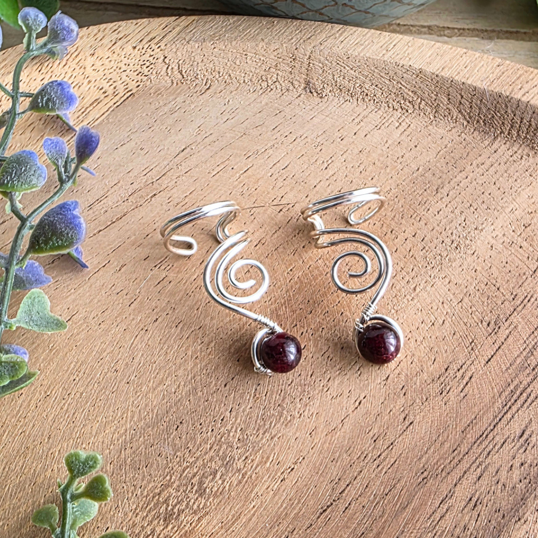 Ear Cuff Vortex Silberfarben Granat auf Holzhintergrund mit lila Blumen
