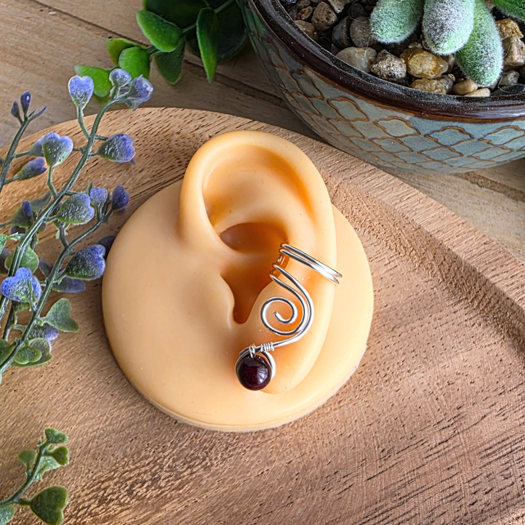 Ear Cuff Vortex Silberfarben Granat auf einem Silikonohr präsentiert