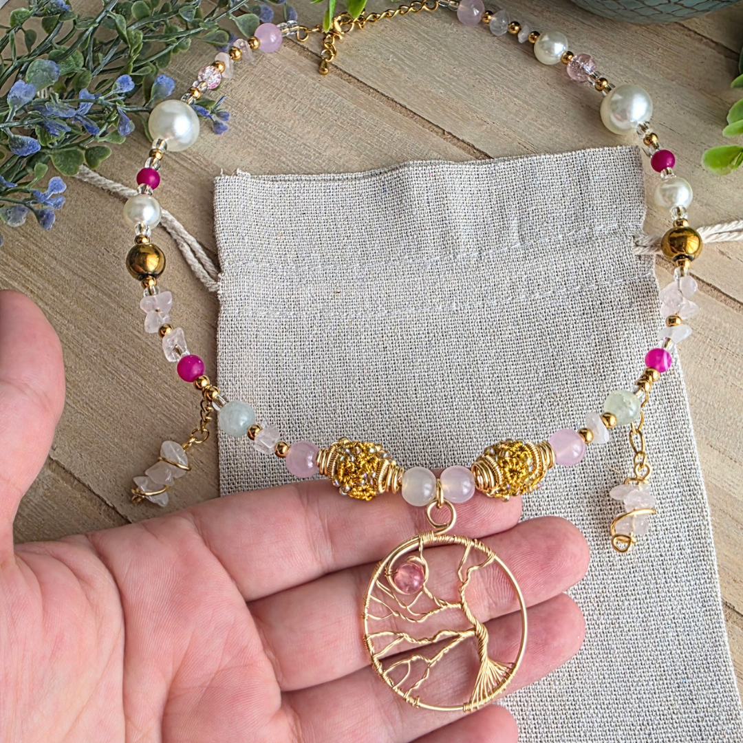 Detailansicht eines Halsreifs mit rosa und grünen Steinperlen, Rosenquarzsplittern, goldfarbenen Perlen und handgearbeitetem Lebensbaum-Anhänger