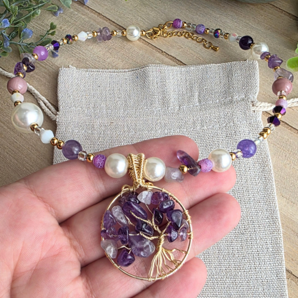 Detailaufnahme eines goldfarbenen Lebensbaum-Anhängers mit violetten Amethystsplittern an einem Halsreif mit weißen Perlen und verschiedenen lila Edelstein- und Glasperlen