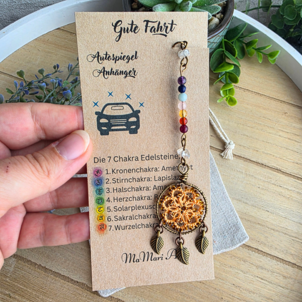 Handgefertigter Chakra Traumfänger fürs Auto in Autumn Orange mit sieben Edelsteinen und drei Blattanhängern auf Produktkarte.