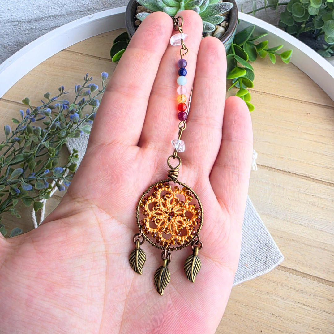 Größenansicht des Chakra Traumfänger Autospiegelanhängers in Autumn Orange mit sieben Edelsteinen und drei Blattanhängern in der Hand.