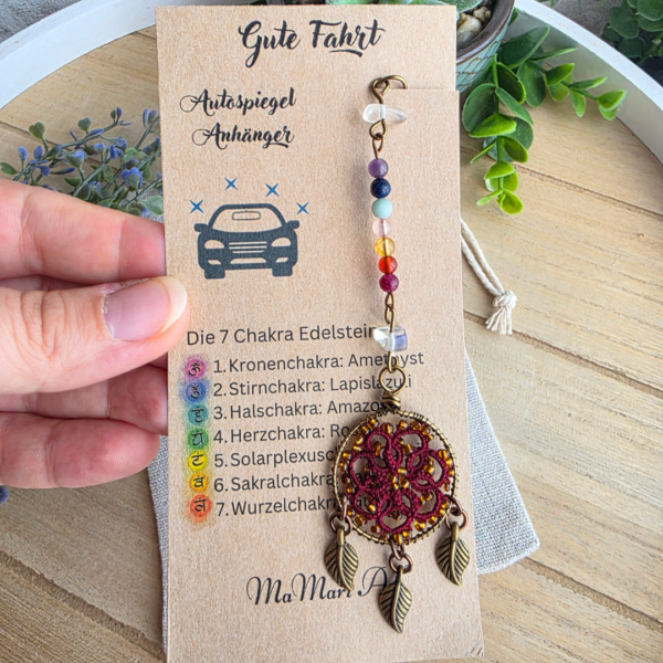 Handgefertigter Chakra Traumfänger fürs Auto in Bordeauxrot mit Edelsteinreihe und drei Blattanhängern auf Produktkarte.