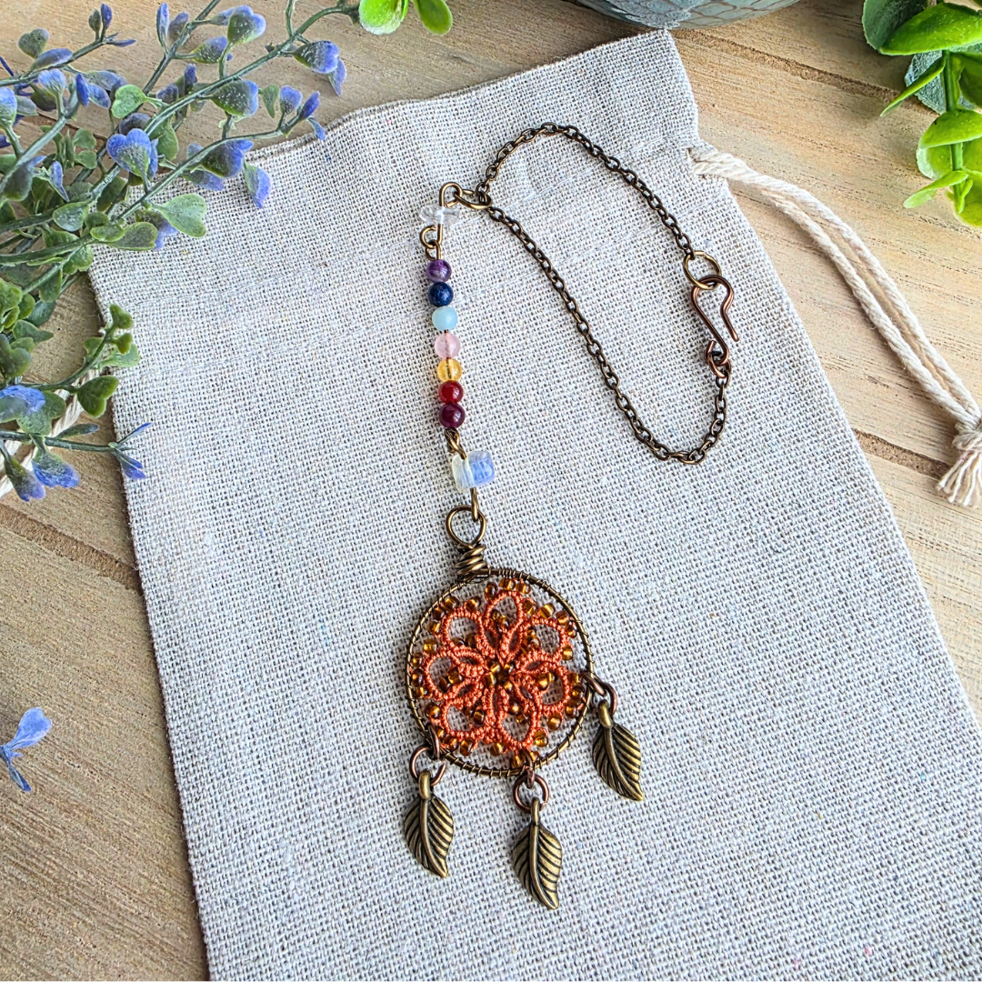 Detailansicht des Autospiegelanhängers mit Occhi-Traumfänger in Harvest Orange, Chakra-Edelsteinen und antikbronzenen Blättern.