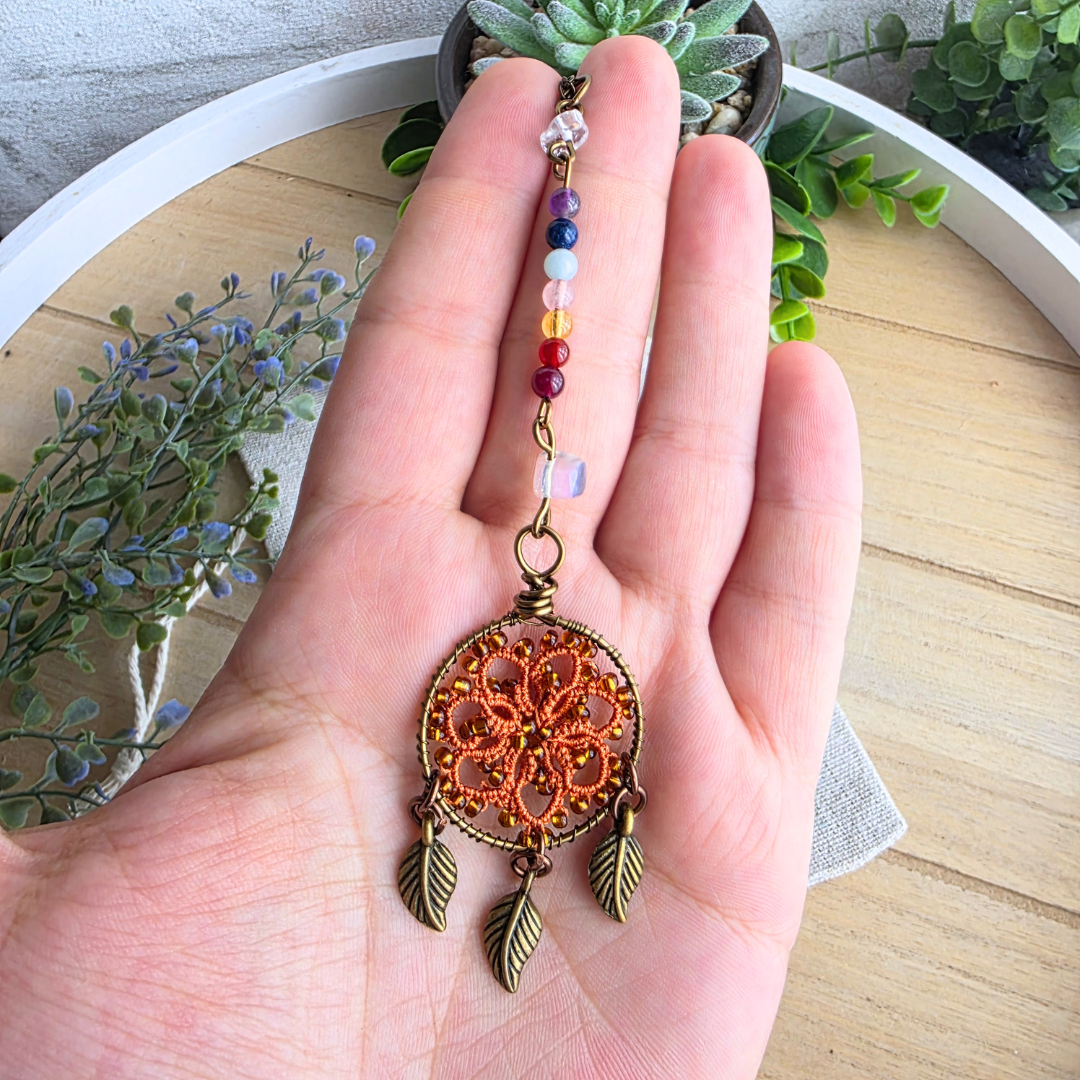 Größenansicht des Chakra Traumfänger Autospiegelanhängers in Harvest Orange mit Edelsteinen und drei Blattanhängern in der Hand.