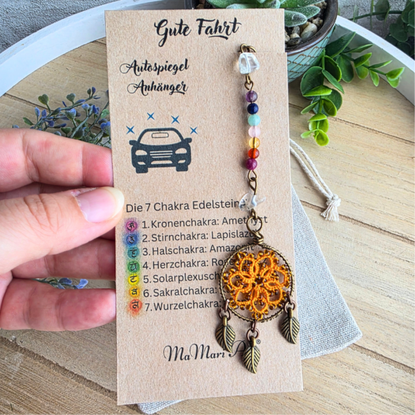 Handgefertigter Chakra Traumfänger fürs Auto in Orange mit Edelsteinreihe und drei Blattanhängern auf Produktkarte.