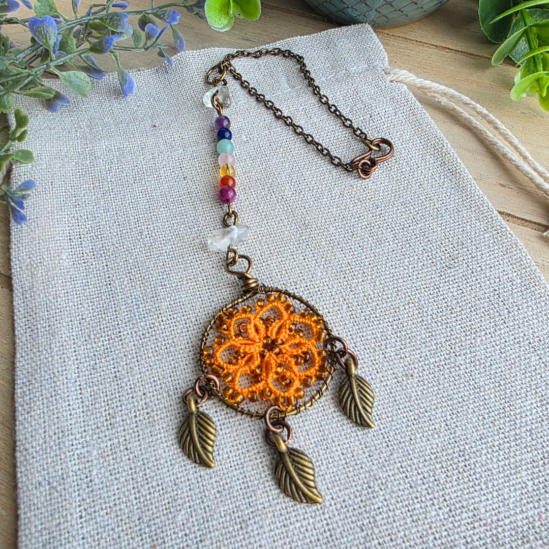 Detailansicht des orangefarbenen Chakra Traumfänger Autospiegelanhängers mit Occhi-Motiv, Edelsteinen und drei Blattanhängern.